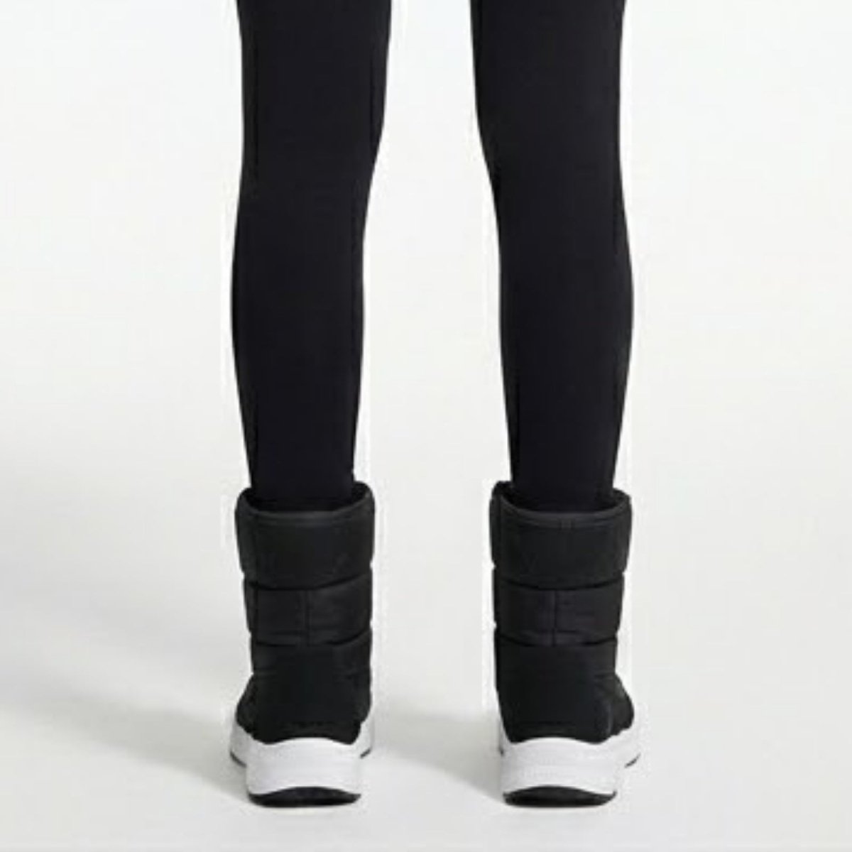 A rear view of a woman wearing black leggings and Kouvr Gianna puffer boots, highlighting the quilted design and heel construction.
