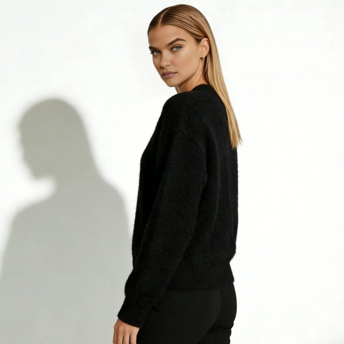 Model looking over her shoulder to show the relaxed fit and soft texture of the Kouvr Gina black mohair-blend cardigan from a three-quarter angle.