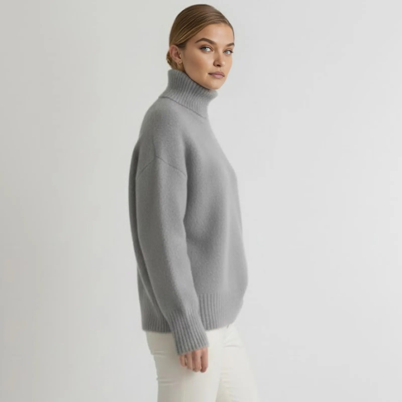 Model wearing the grey oversized cashmere turtleneck sweater from the side, showcasing its relaxed fit and drape.