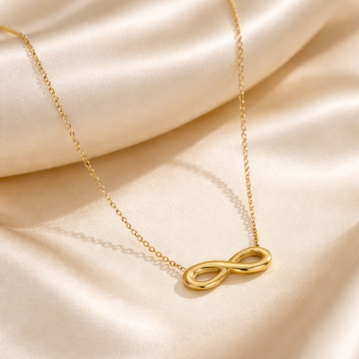 Close-up of the handmade Kouvr gold infinity necklace resting on a luxurious silk fabric.