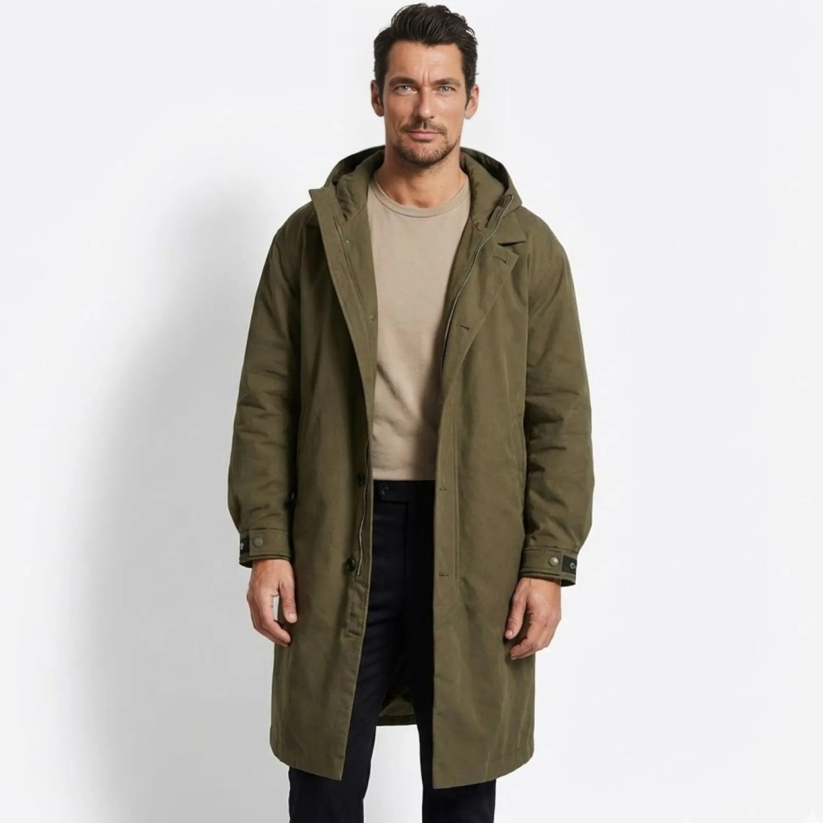 Man wearing the Kouvr Hartley men's long hooded parka in army green, styled with a beige t-shirt and black pants.