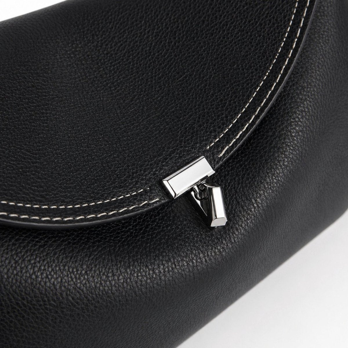 A close-up detail shot of the custom silver T-clasp hardware and the fine white contrast stitching on the flap of the black leather Kouvr Iscah bag.