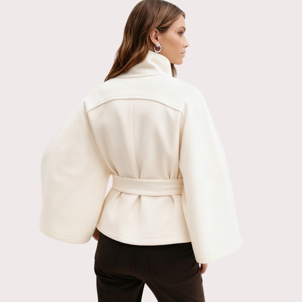 Model facing forward wears the Kouvr Jaye white wool belted cape coat with a high funnel neck and wide kimono sleeves