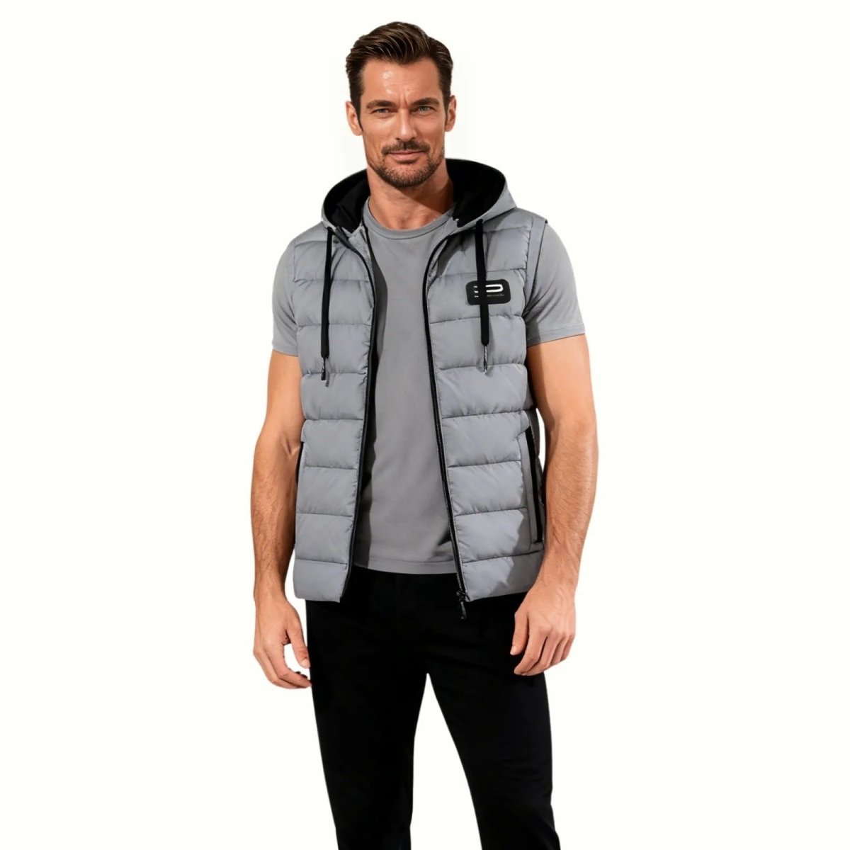 Male model wearing the slate grey Kouvr Jomari Hooded Puffer Vest over a grey t-shirt and black pants, shown from the front against a white background.