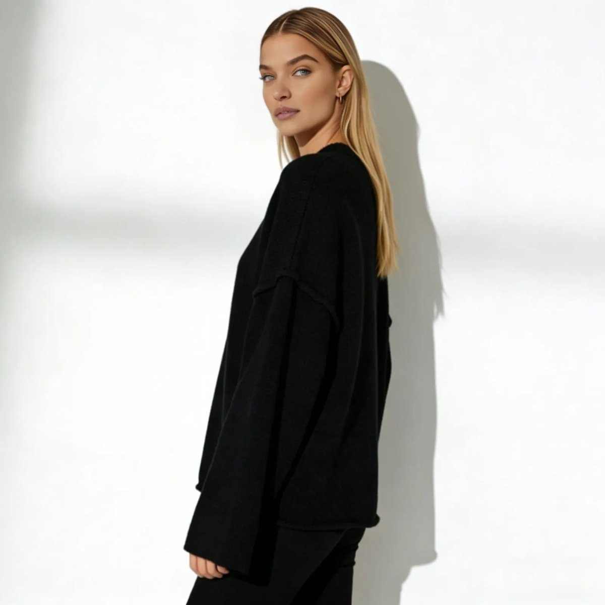 Side profile of a woman in an oversized black wool and cashmere blend sweater, highlighting the dramatic flared sleeve silhouette.