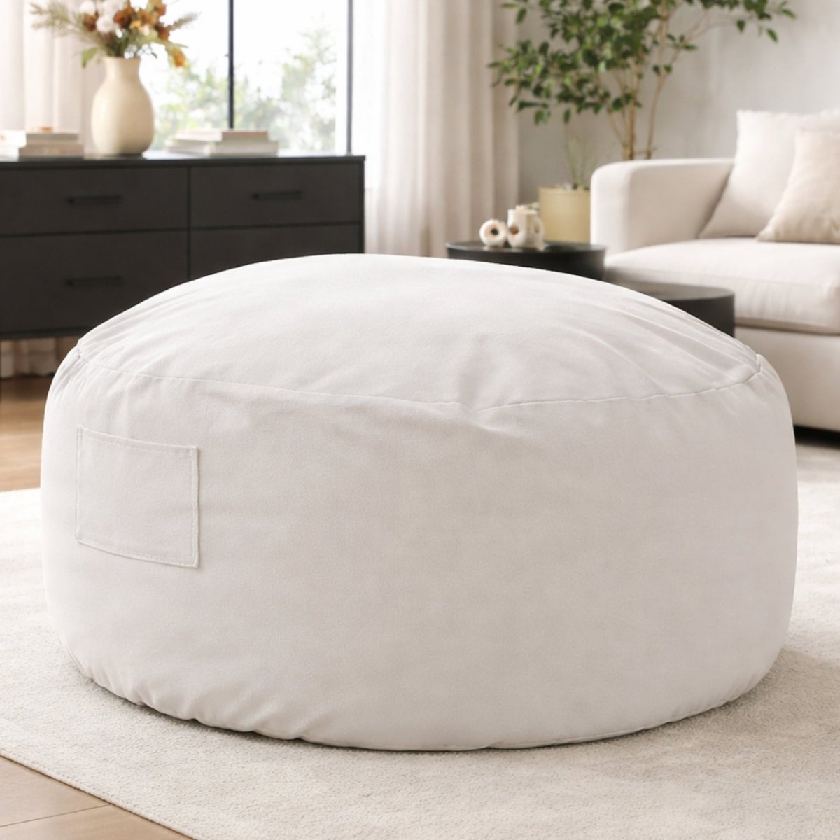 Large light grey memory foam bean bag chair by Kouvr, placed on a beige rug in a bright, contemporary living room.