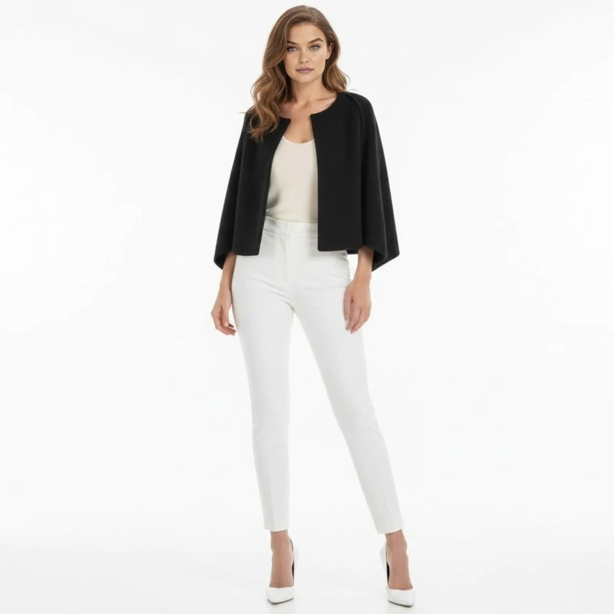 A woman models the Kouvr Laverne structured cropped cape jacket in black, styled with a white top and white tailored trousers.