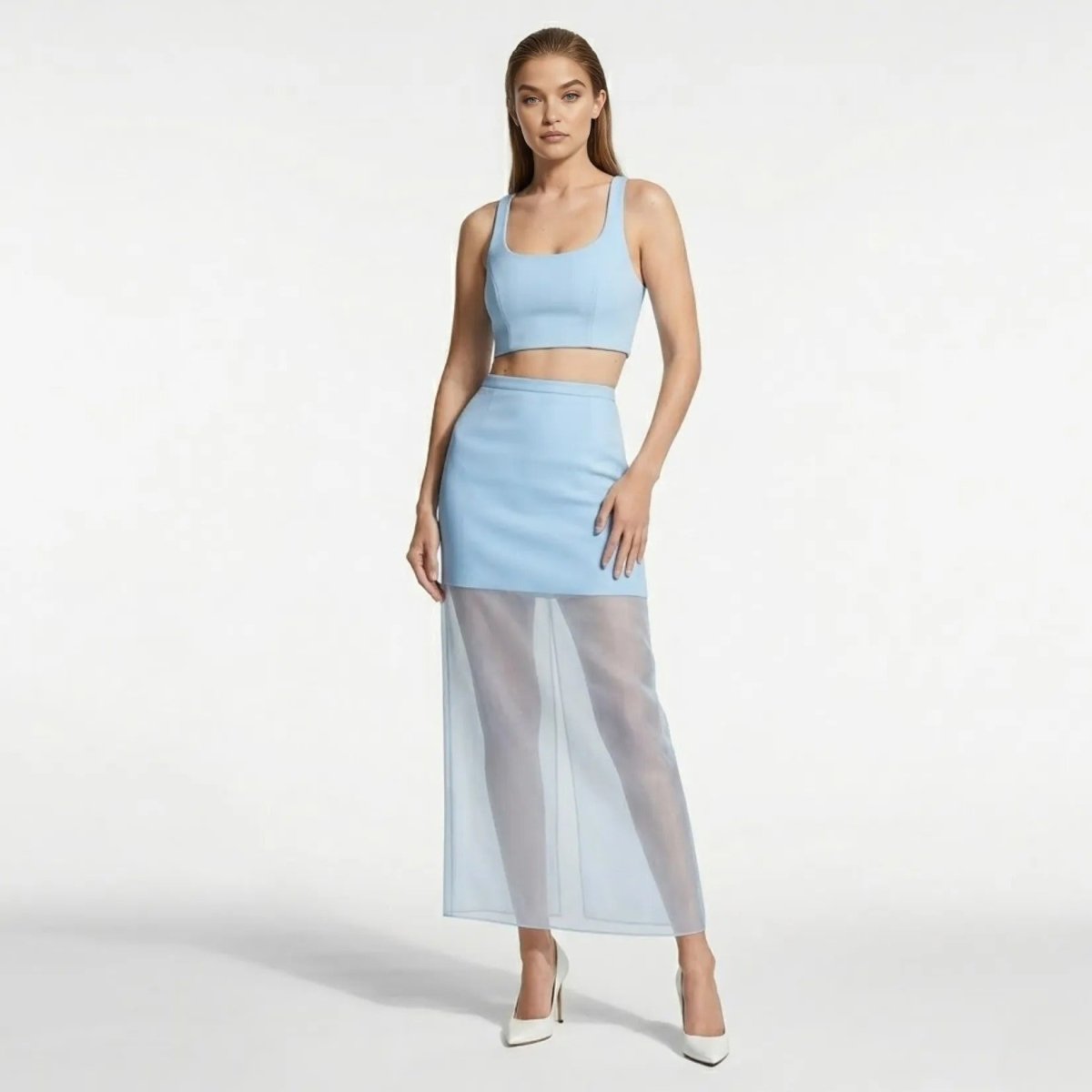 Model wearing an elegant light blue designer cocktail skirt with a transparent maxi hem paired with a matching crop top and white heels.