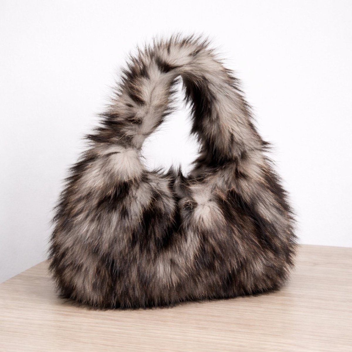 Close-up detail shot of the Kouvr Linnea Wolf Faux Fur Bag on a wooden surface, showing its soft, luxurious texture.