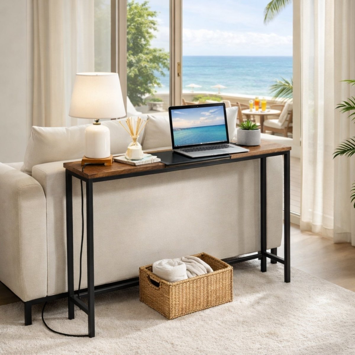 Kouvr 64 inch extra long console table styled behind cream sofa with laptop and lamp, ocean view background.