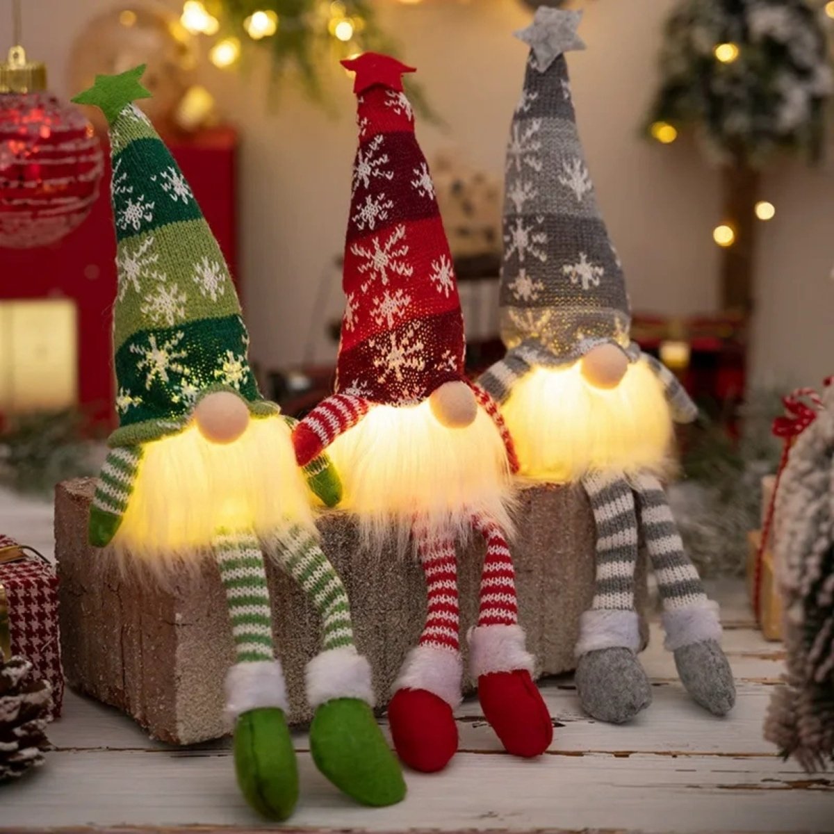 Side profile of three Kouvr lighted Christmas gnomes sitting on a wooden block, featuring their striped dangling legs and the ambient light from their bodies illuminating the scene.