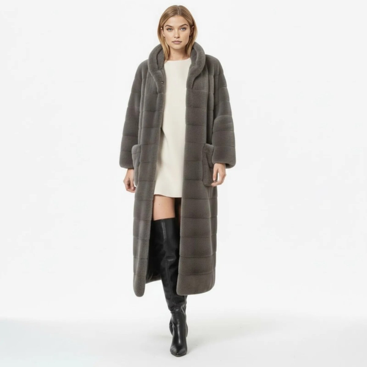 Model wearing the Luisa long grey hooded faux fur coat from Kouvr, styled with a white dress and black knee-high boots.