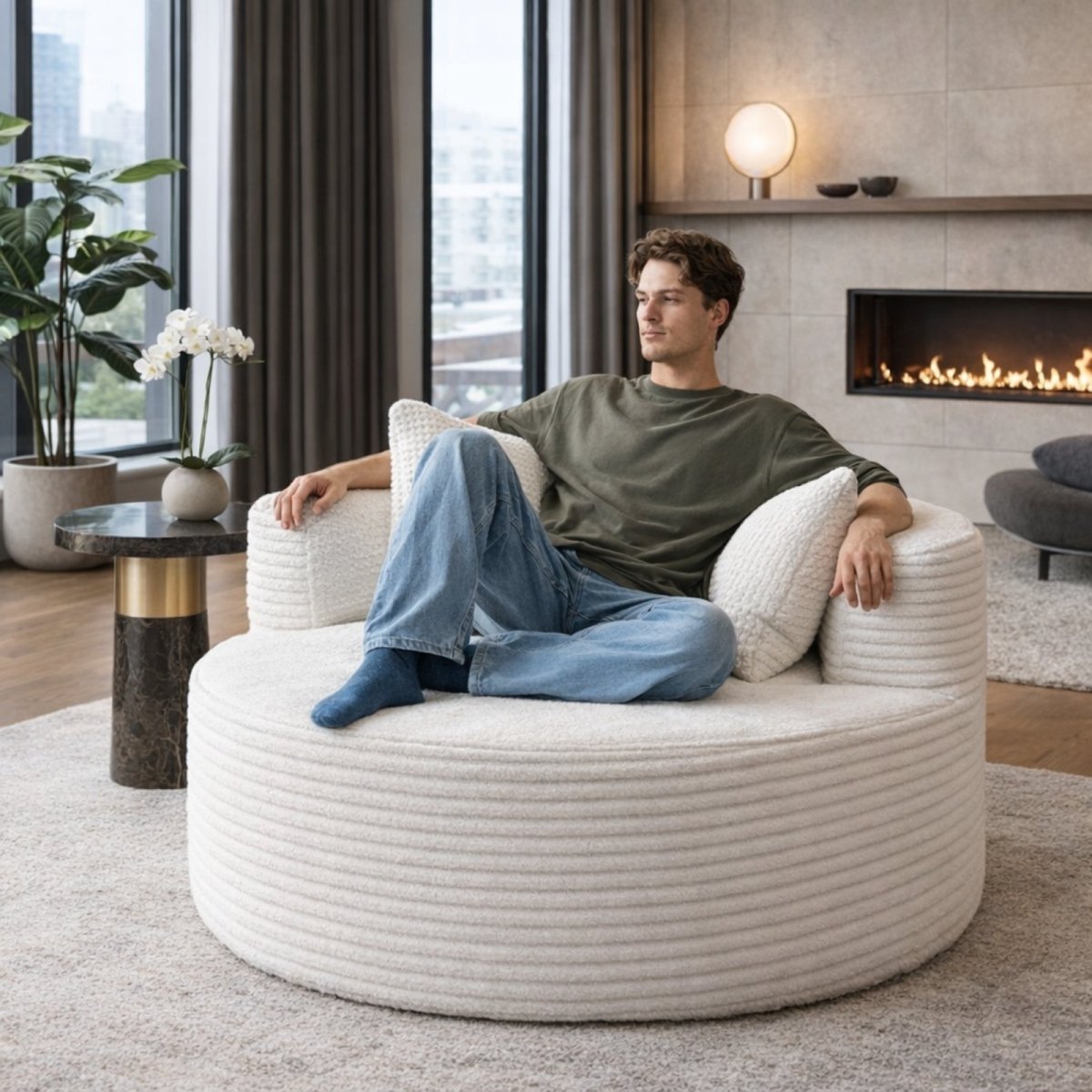 Man sitting comfortably cross-legged on Kouvr white oversized swivel chair, demonstrating spacious 50 inch wide seating capacity and cloud-like comfort.