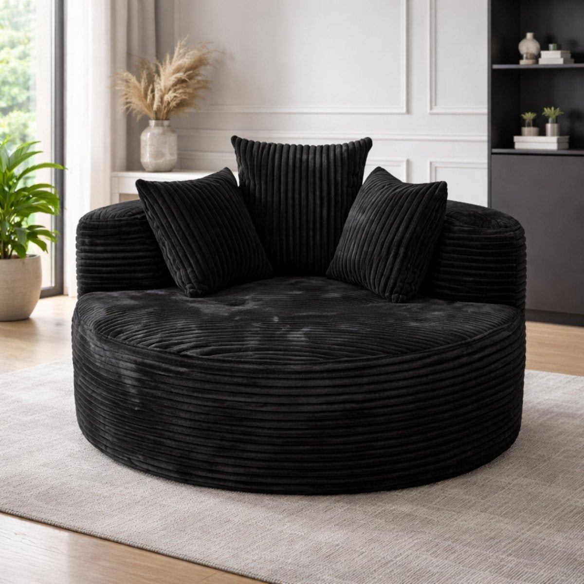 Black corduroy oversized barrel chair with three plush pillows, modern luxury circular seating for reading nook or bedroom.