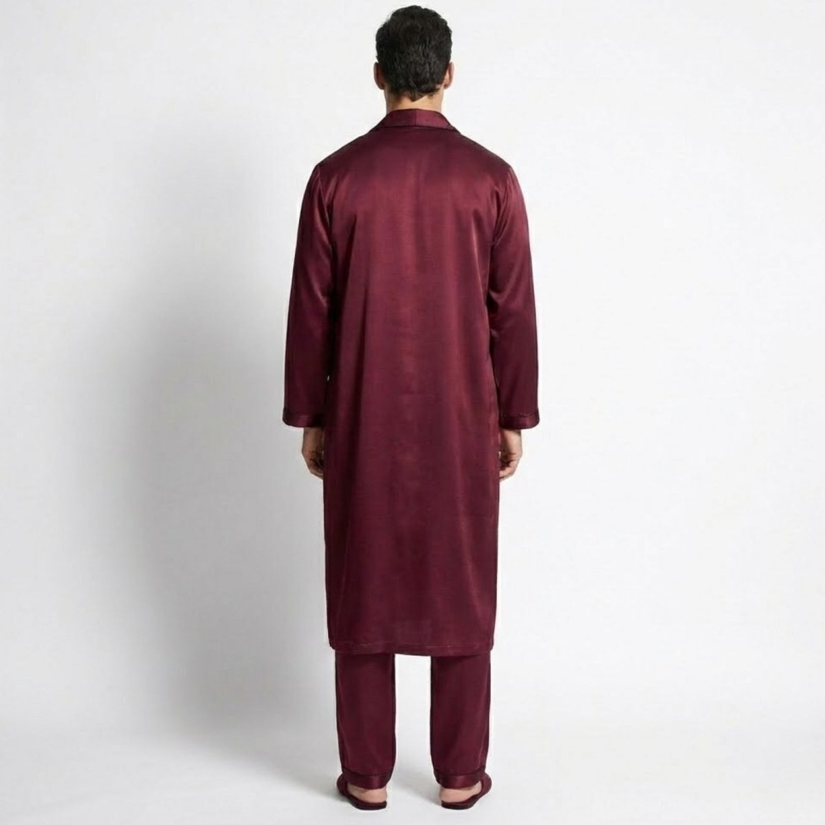 Back view of a male model wearing the Kouvr long burgundy silk robe over matching pajamas.
