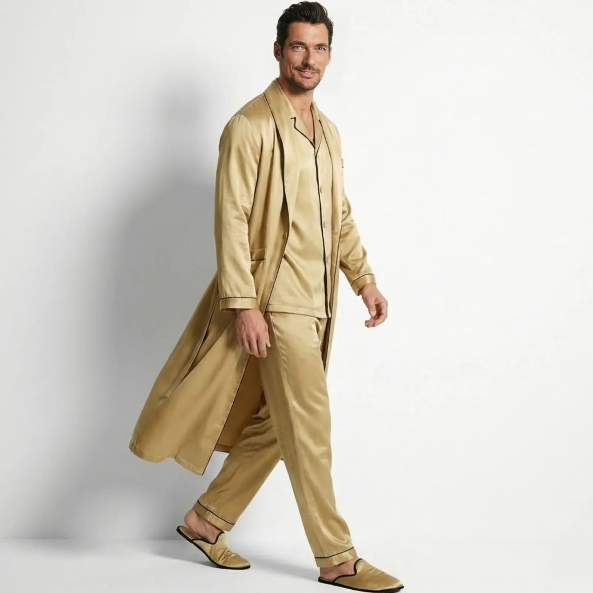 Male model in a side profile view, walking in the Kouvr gold satin pajama set, showing the flow and drape of the long robe.
