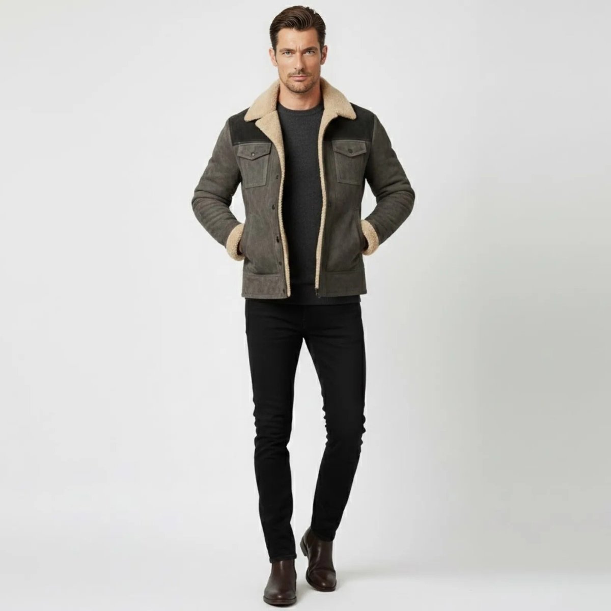 Male model wearing the Kouvr grey suede shearling jacket with a dark sweater and black jeans, showing the front view with hands in pockets.