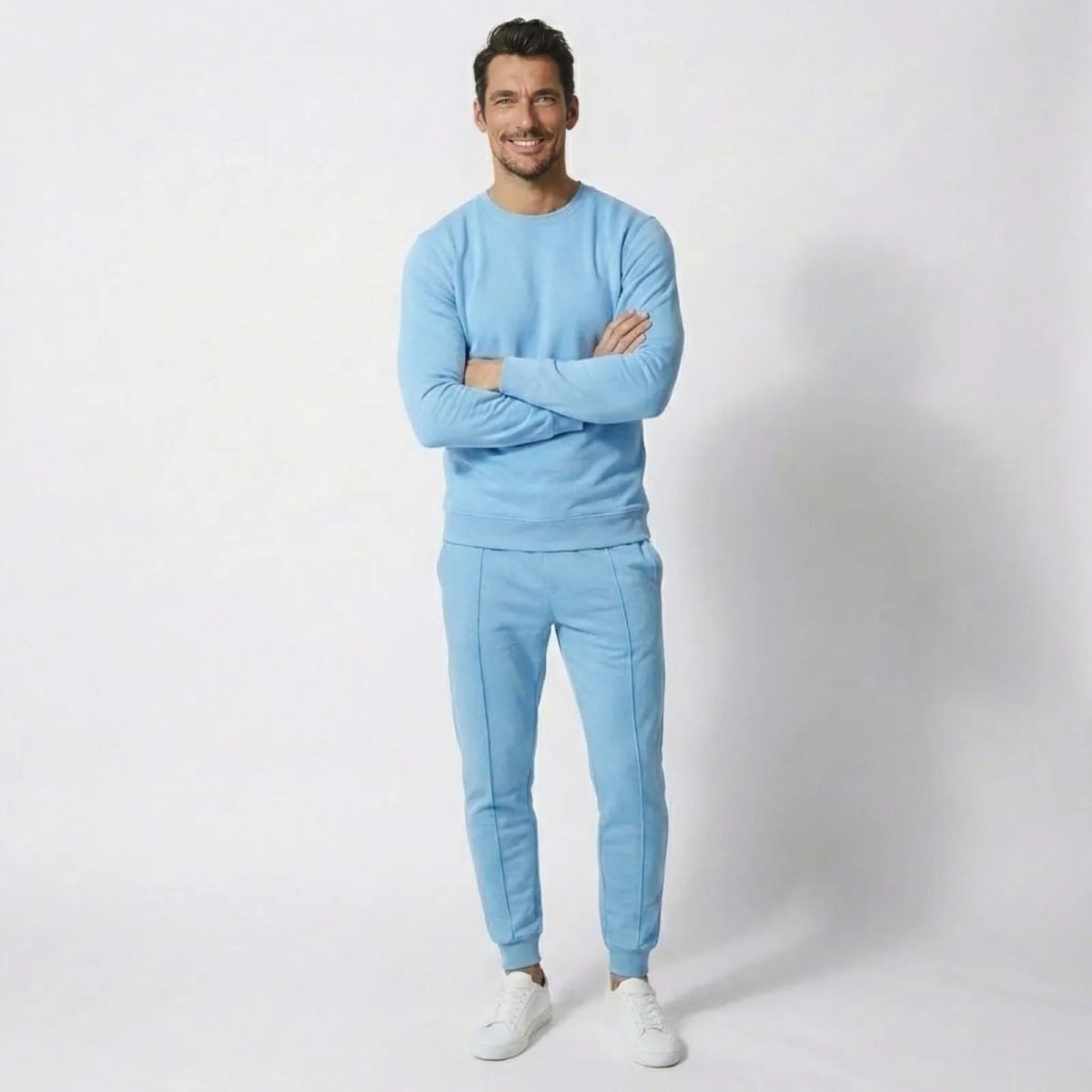 Male model wearing Kouvr's light blue luxury tracksuit set, standing front-on with arms crossed against a white background.
