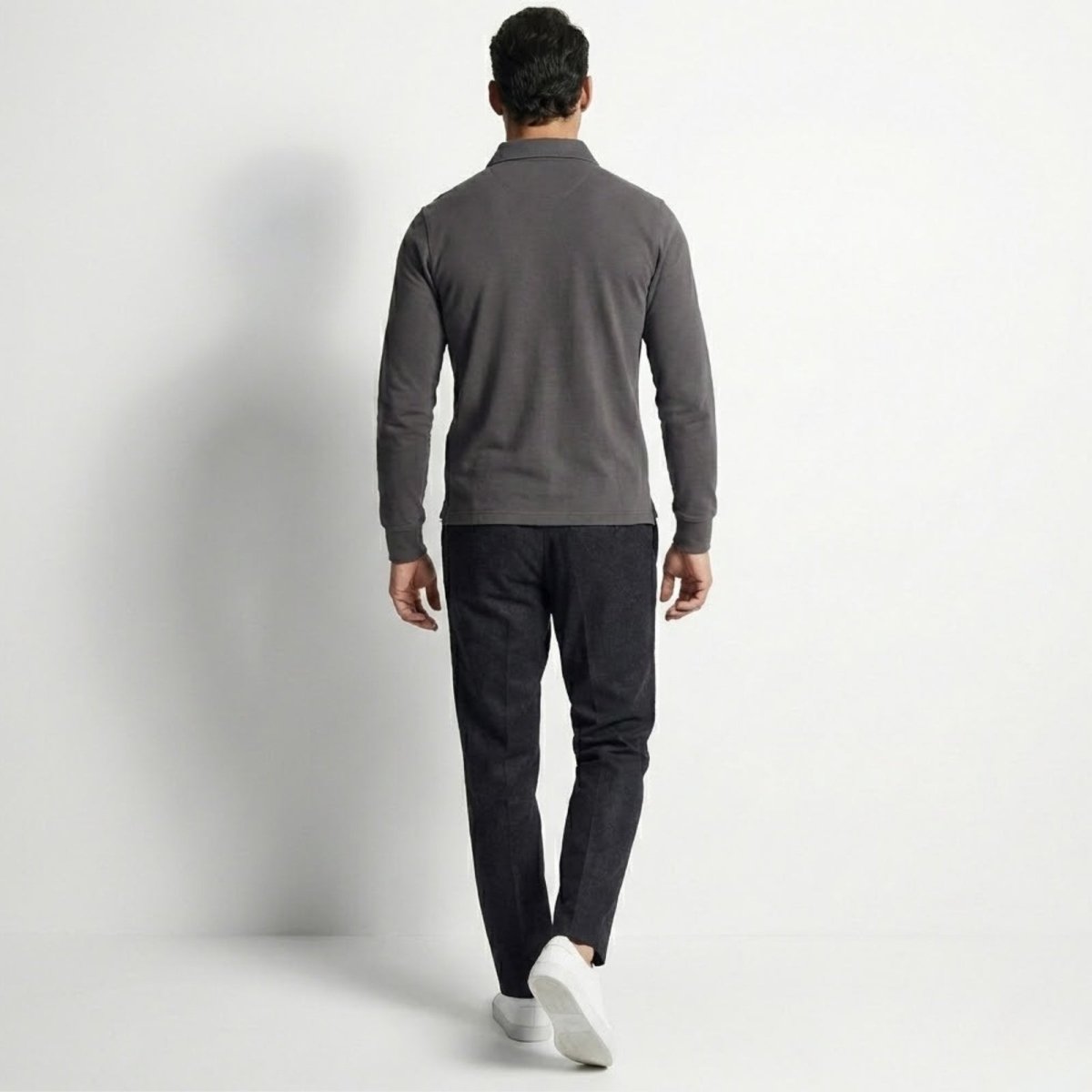 Back view of a man wearing the Kouvr slim fit long sleeve polo shirt in a dark charcoal grey color.