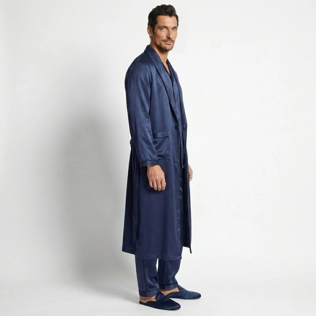Side profile of a model in a Kouvr long navy satin robe and pajama set, showing the garment's length and drape.