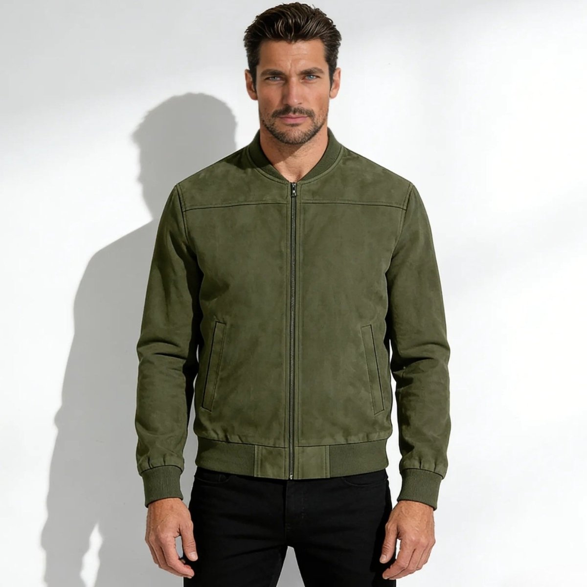 Man wearing the Kouvr luxury olive green suede bomber jacket with black jeans against a white background.