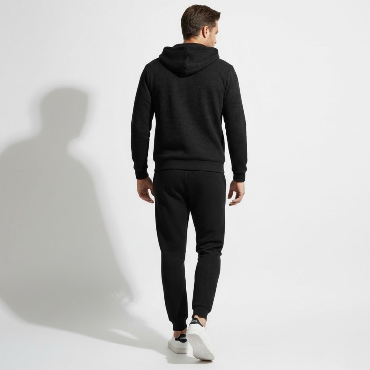 Back view of a male model wearing the complete Kouvr black waffle-knit tracksuit, showing the fit of the hoodie and joggers.