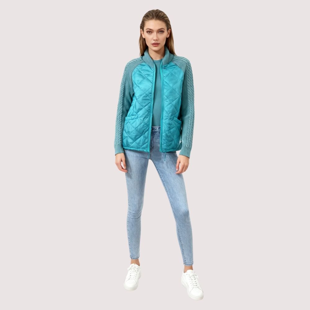 Model wearing the Kouvr Mika Hybrid Bomber Jacket in Aegean Teal, featuring cable-knit sleeves and a diamond-quilted body, paired with light-wash skinny jeans and white sneakers