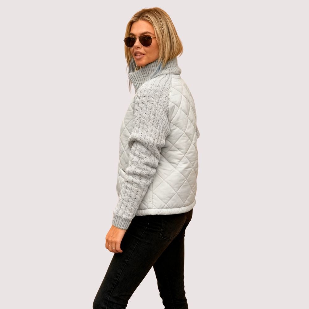 Model wearing the Kouvr Mika hybrid jacket in Heather Gray and Winter White, featuring quilted body and honeycomb knit sleeves, styled with black jeans and sunglasses