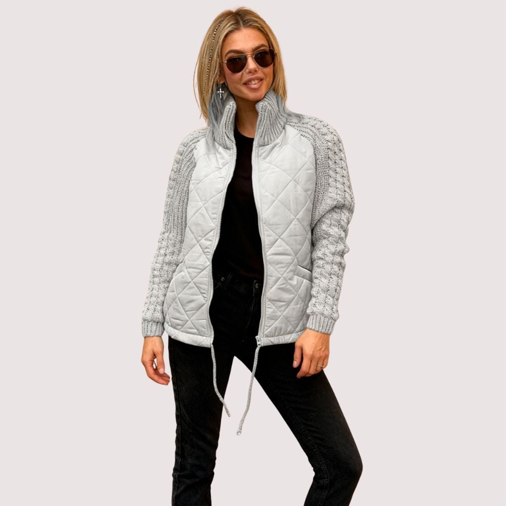 Model wearing the Kouvr Mika hybrid jacket in Heather Gray and Winter White, featuring quilted body and honeycomb knit sleeves, styled with black jeans and sunglasses
