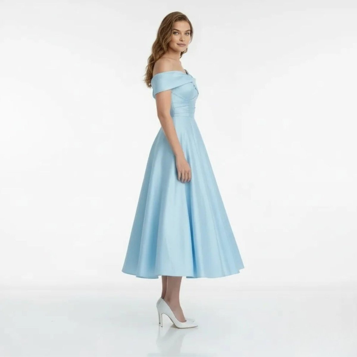 Side profile of a model in the Kouvr Nadine light blue tea-length dress, showing the A-line silhouette and off-shoulder design.