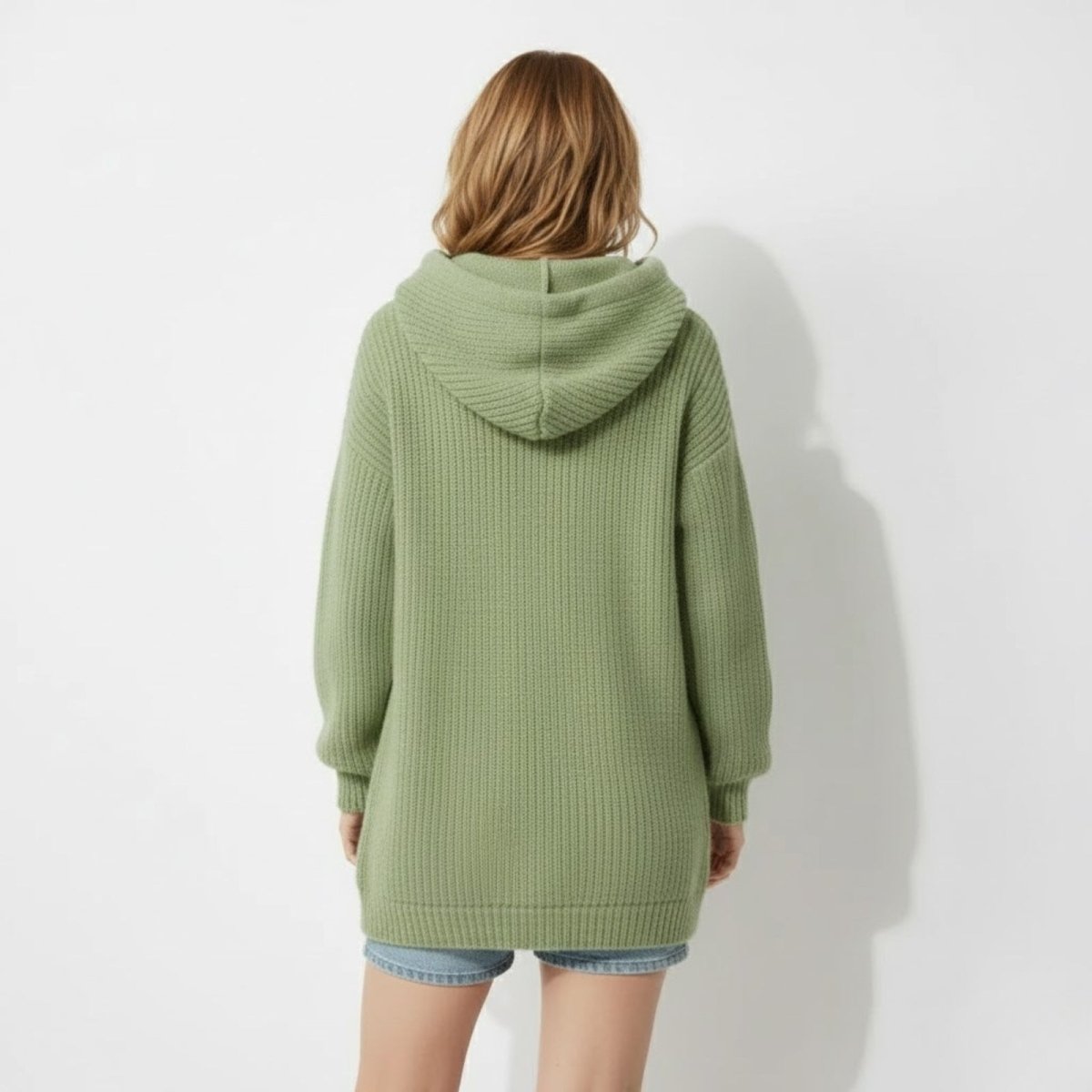 Back view of model wearing the Kouvr Nadya oversized chunky knit hoodie in green, showcasing the hood and relaxed fit.