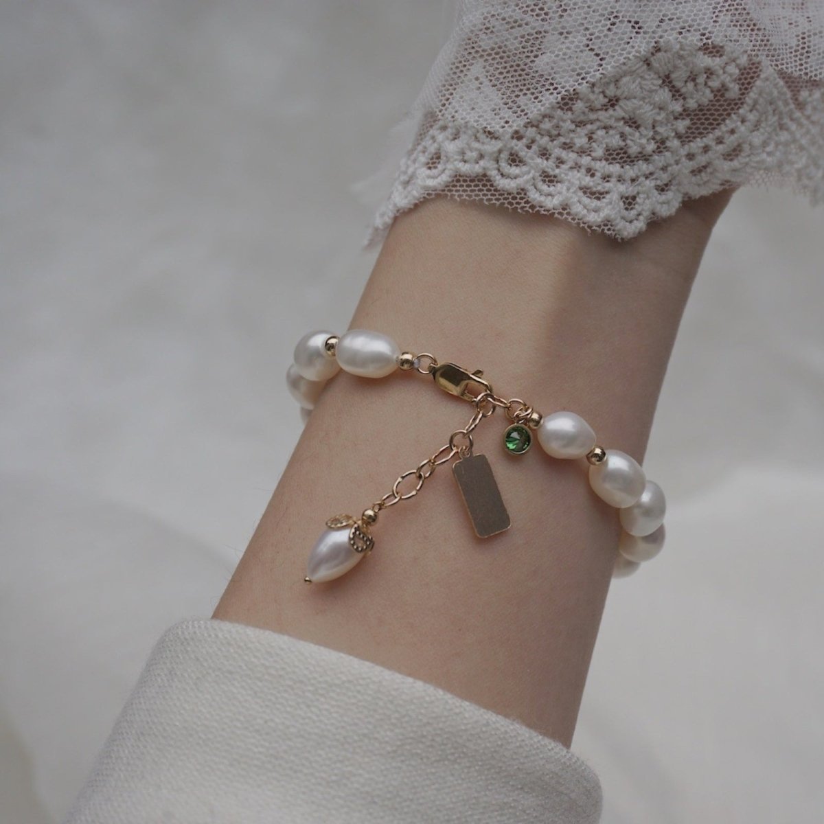 A woman wearing the Nathalia Freshwater Pearl Bracelet, showcasing its elegant fit and gold charm details against her skin