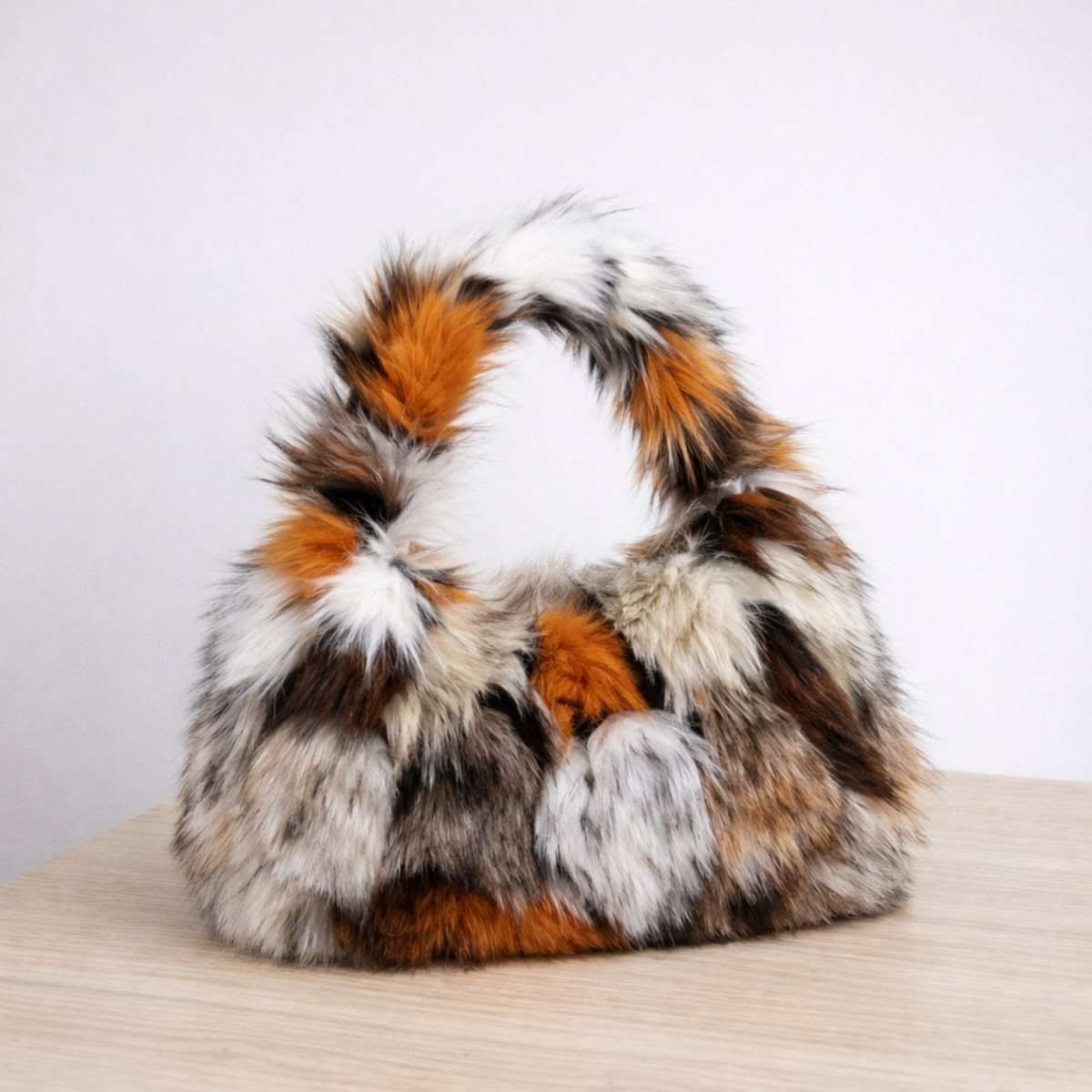 A detailed side view of the Kouvr Nerrisa tortoiseshell faux fur bag resting on a light wood surface, highlighting its fluffy texture.