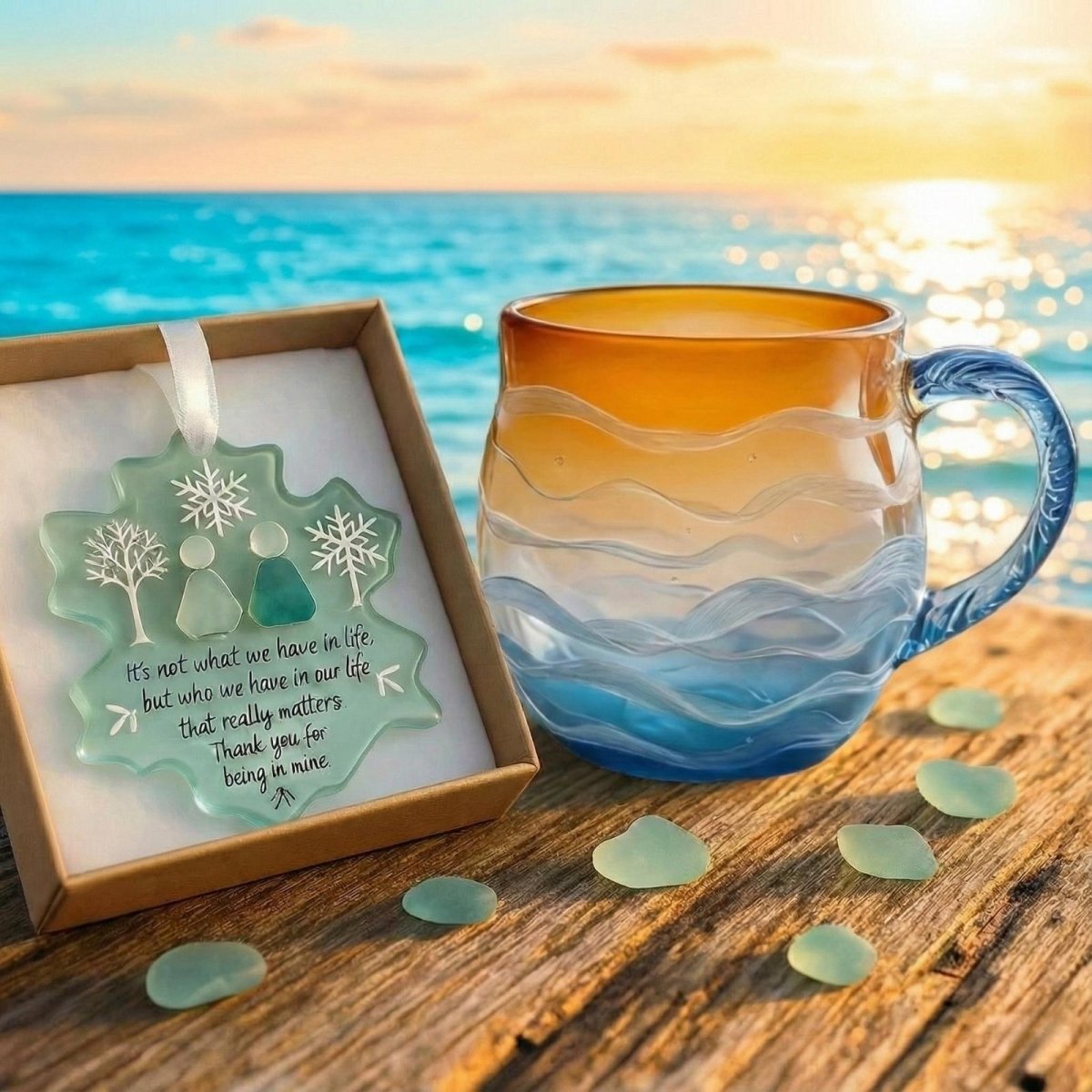 Kouvr's hand blown ocean sunset mug and sea glass snowflake ornament gift set resting on a wooden dock with the ocean in the background.