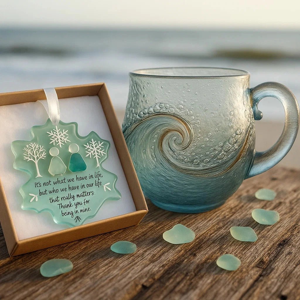 The Kouvr artisan ocean wave glass mug sitting on a rustic wooden plank at the beach with the sea in the background.