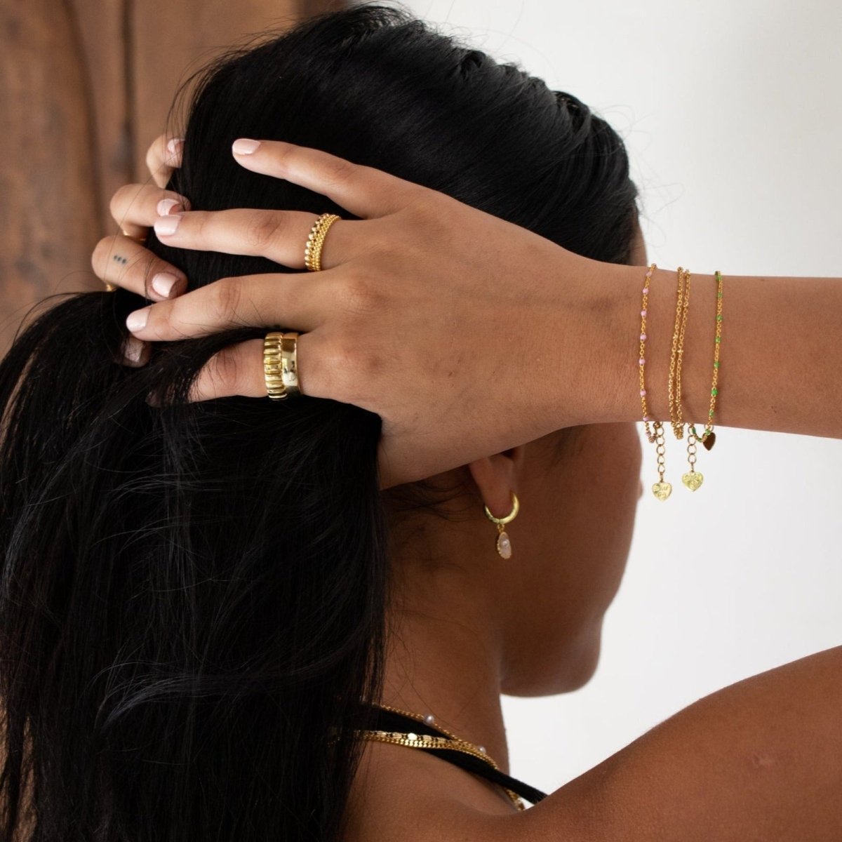 A woman's wrist adorned with the Kouvr Palfi double strand gold bracelet, styled with a necklace.