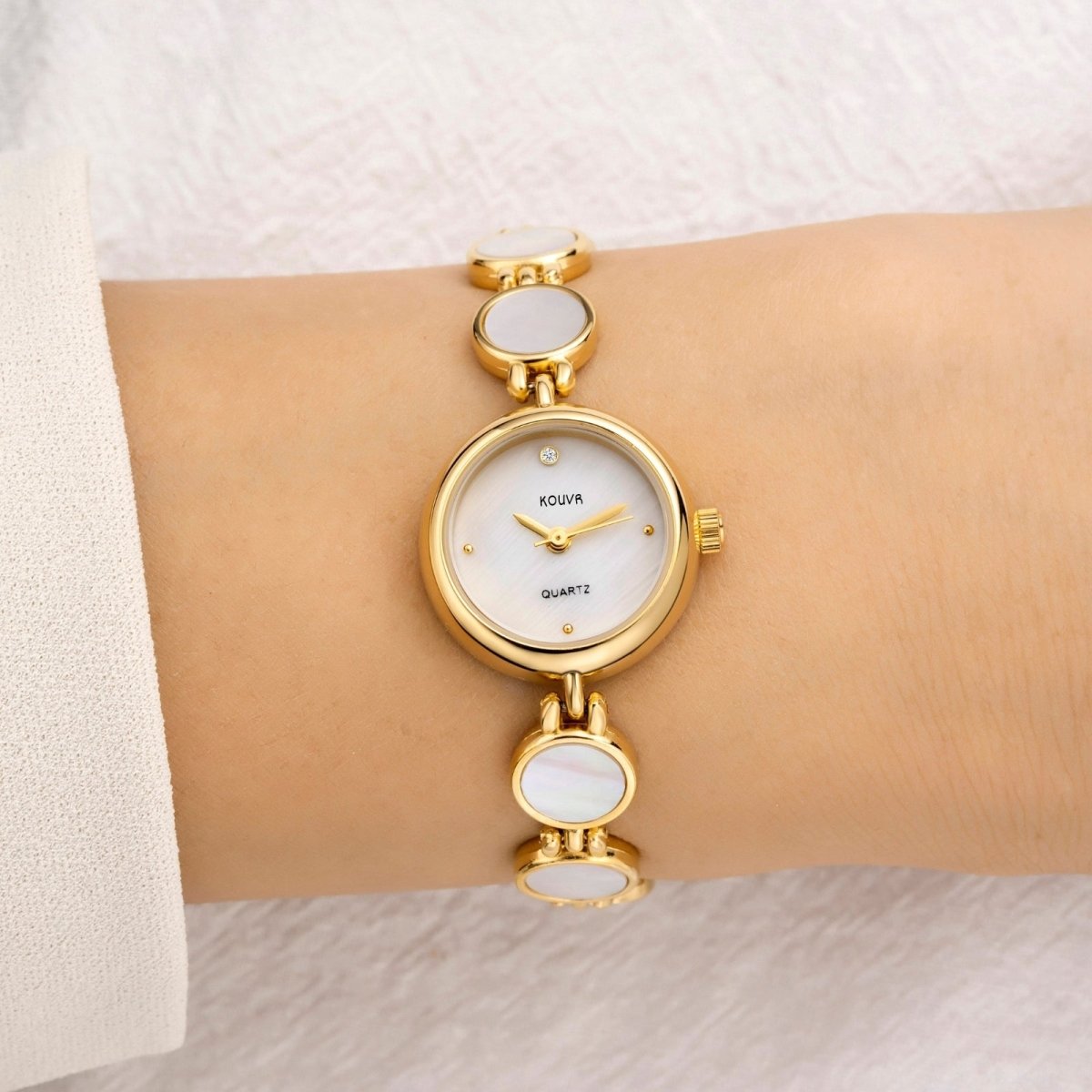 A woman wearing the Kouvr Pearl Faelan gold-tone watch with a white mother of pearl bracelet and dial.
