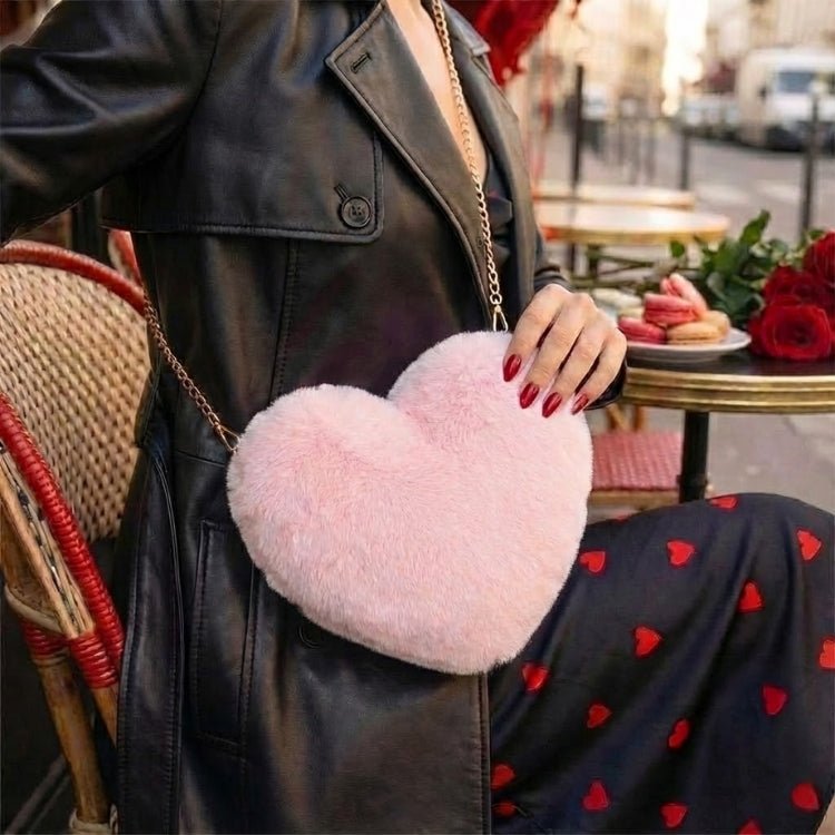 A stylish woman wearing a black leather trench coat with a pink fluffy heart-shaped crossbody bag sitting at an outdoor Parisian cafe