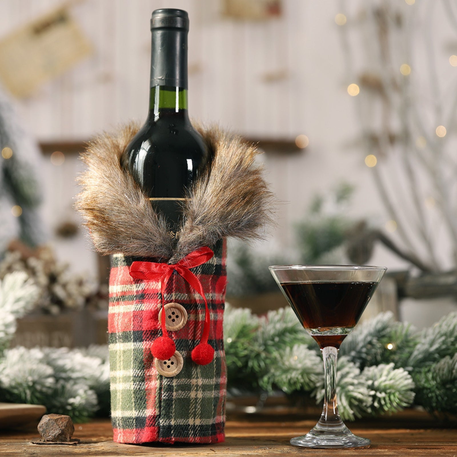 Close-up of a red wine bottle in a festive red and green plaid coat cover with a faux fur collar and red pom-pom tie, part of a luxury tablescape.