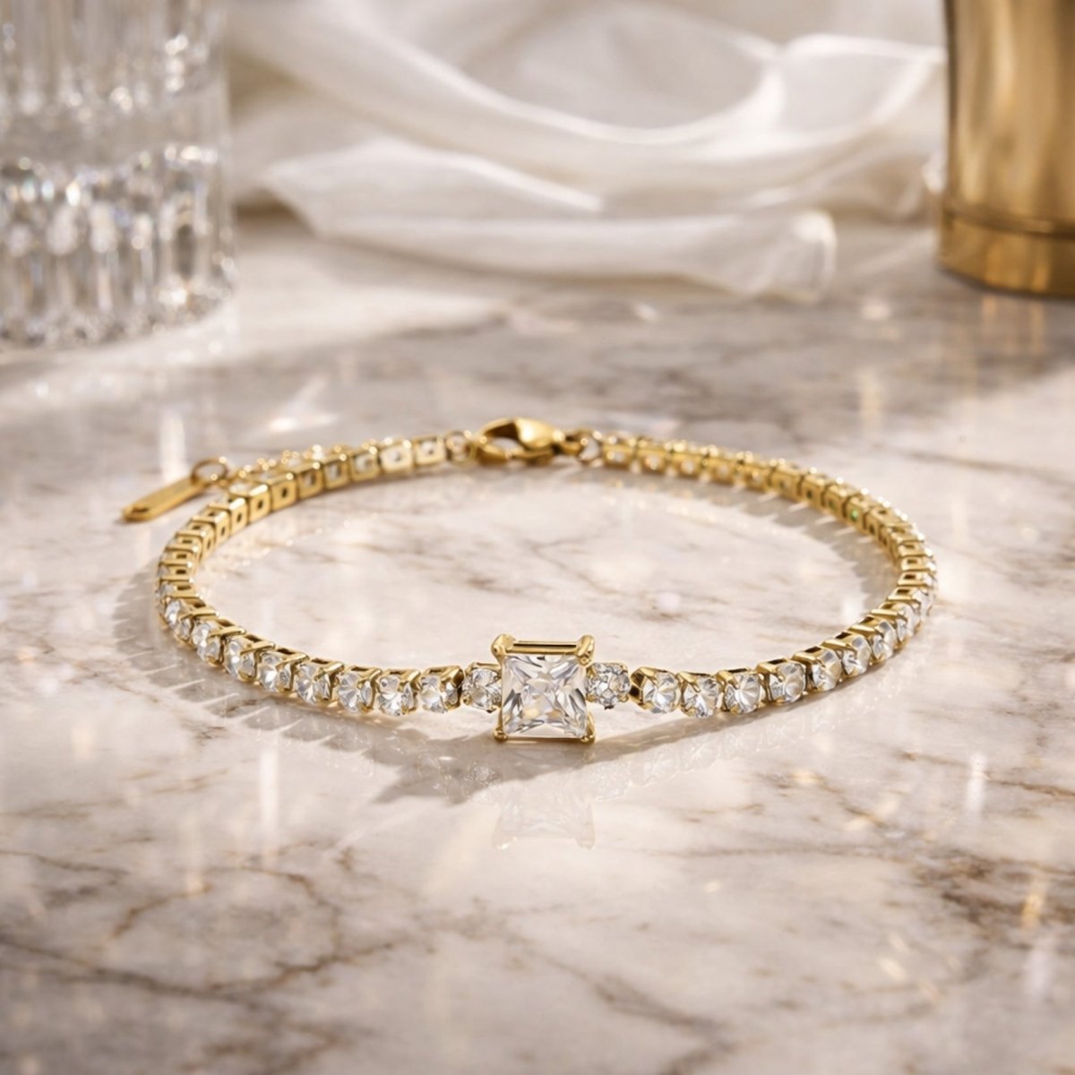 The Kouvr adjustable gold tennis bracelet laid out on a marble surface, highlighting the clasp and extender chain.