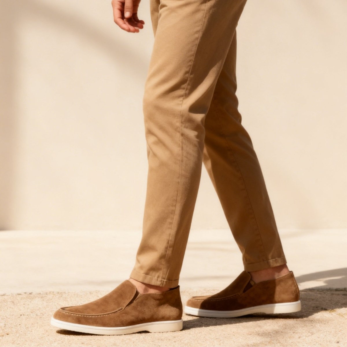 Kouvr suede ankle loafer boots with tan chino pants.
Side view of black Italian suede slip-on boots with a contrasting white sole, worn by a model.
