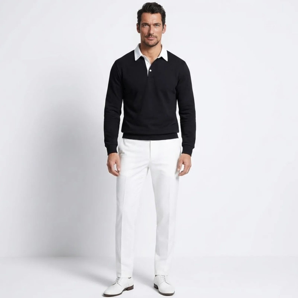 Male model wearing the Kouvr Rhodes black long sleeve knit polo sweater with a white contrast collar, paired with white trousers.
