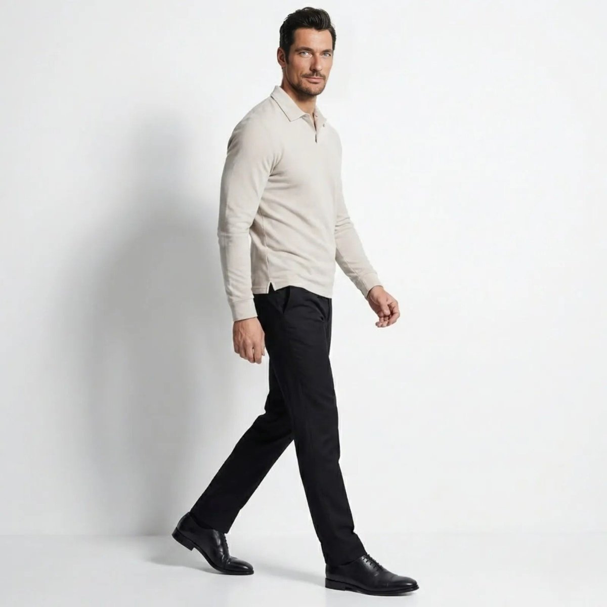 Man in a side profile walking pose wearing a slim fit cream long sleeve knit polo and black dress pants.