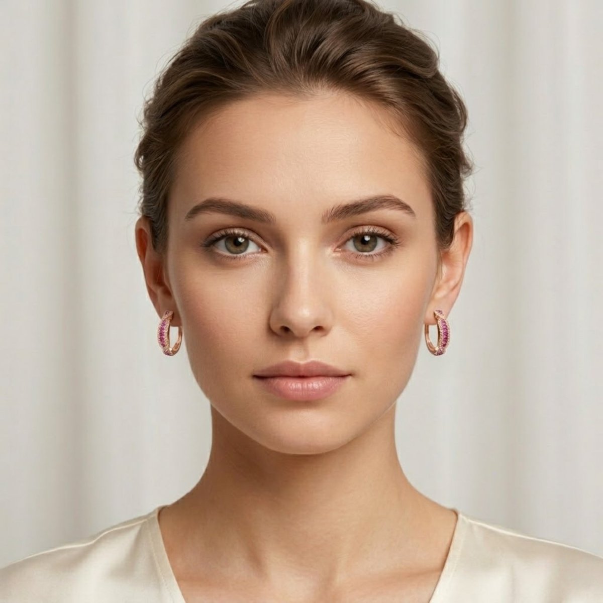 A female model with her hair in a bun wearing Kouvr's 18k rose gold ruby and diamond infinity hoop earrings, showcasing their size and scale.