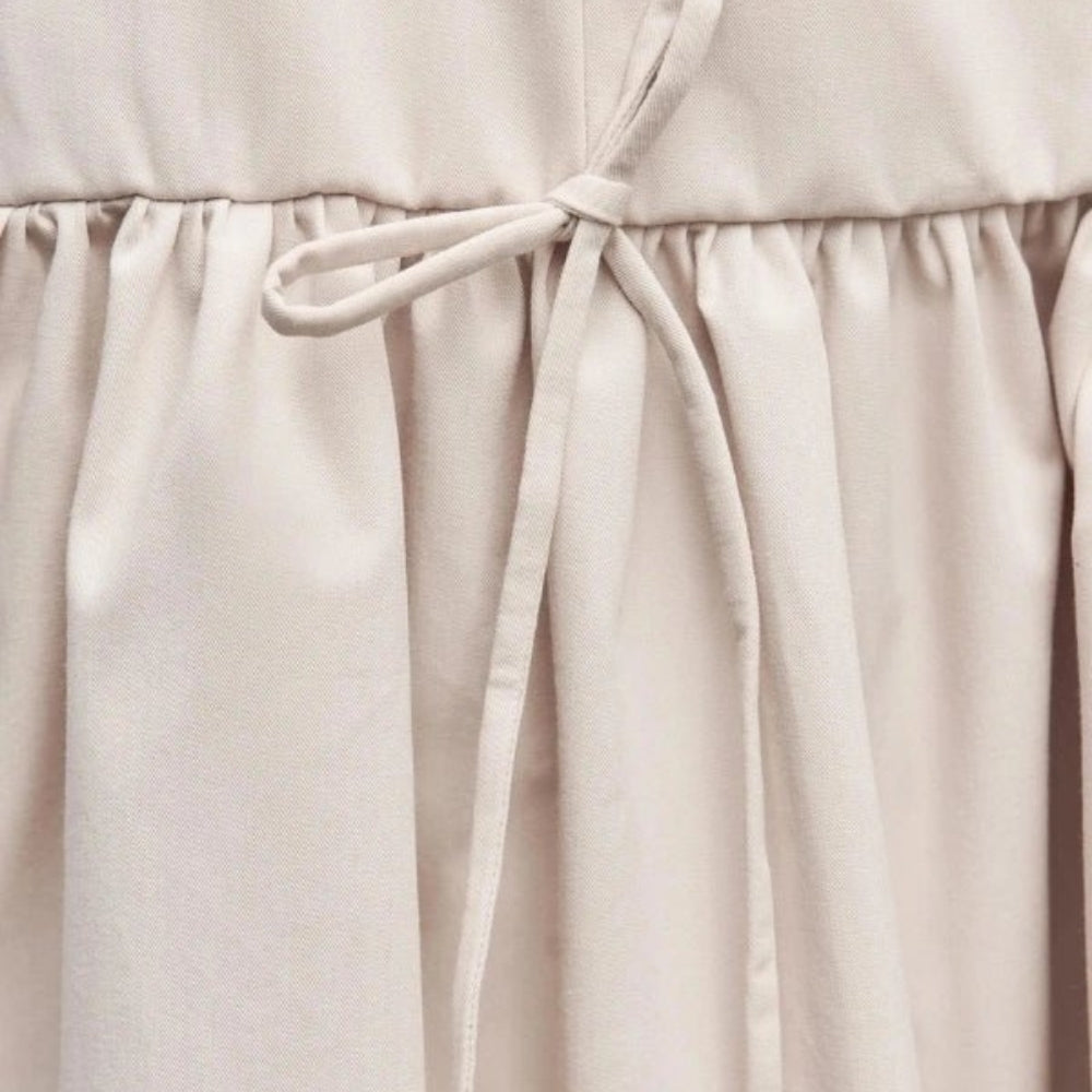 Close-up of a ivory Kouvr dress with a tie waist on a neutral background