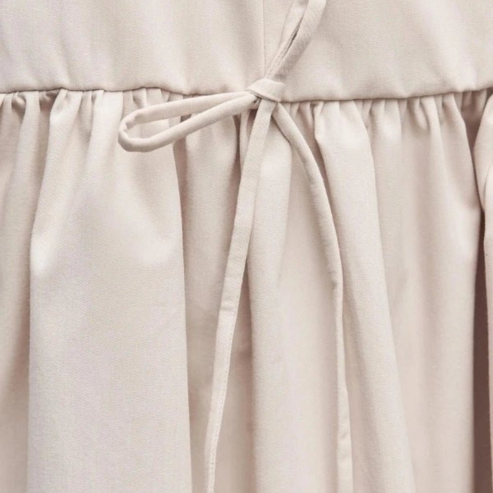 Close-up of a ivory Kouvr dress with a tie waist on a neutral background