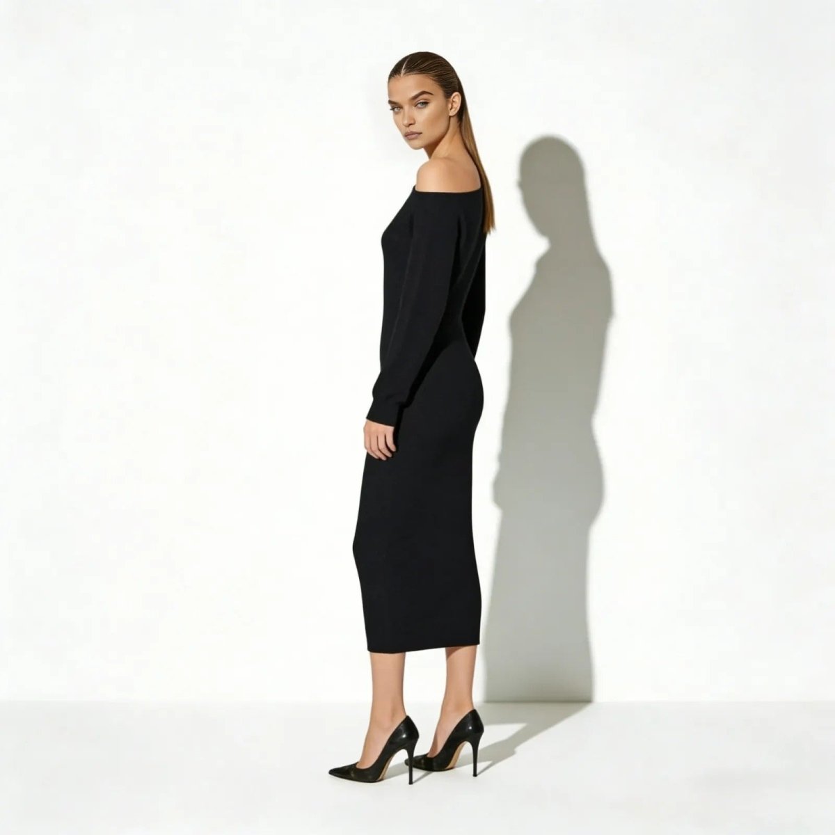 Side profile of a woman in a long-sleeve asymmetrical black sweater dress showing its bodycon silhouette.