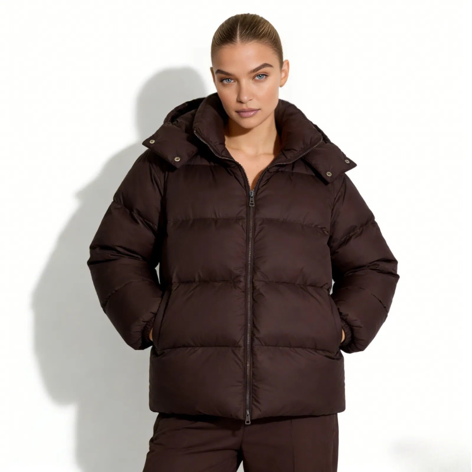 Model wearing the Kouvr Sheena hooded puffer jacket in a rich dark brown, zipped up with hands in pockets.