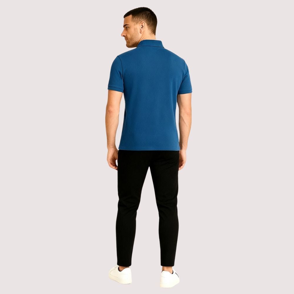 Man wearing a blue kouvr polo shirt and black pants on a light gray background