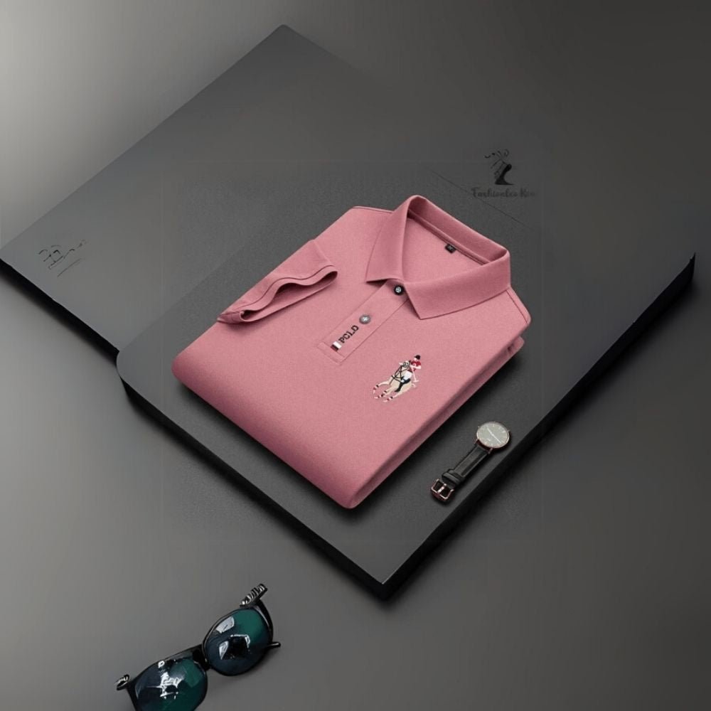 Pink kouvr polo shirt with brand logo on a dark surface, accompanied by sunglasses.